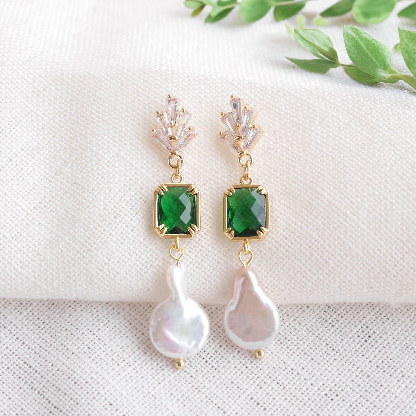 Green art deco style dangle earrings on a white cloth.