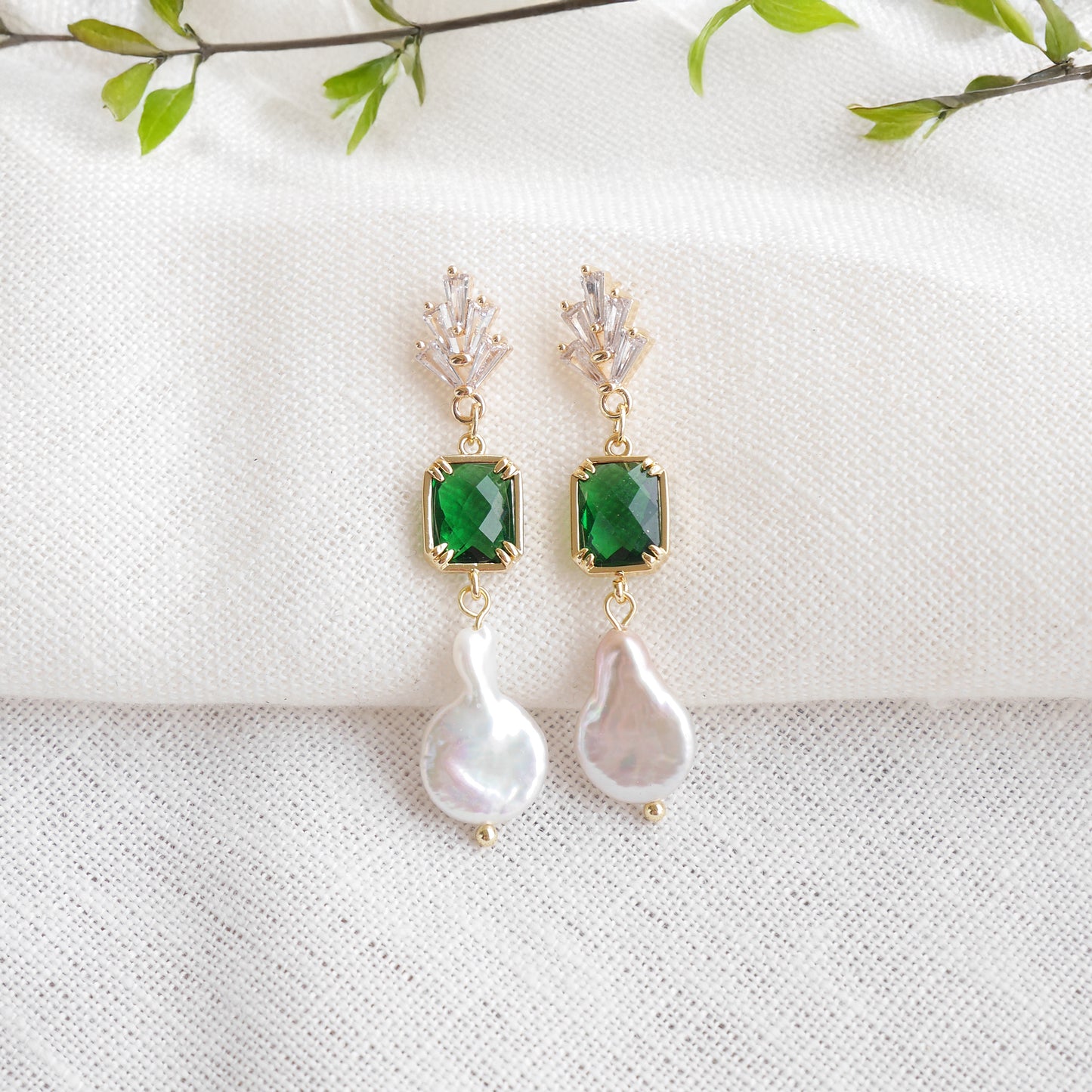 Green art deco style dangle earrings on a white cloth.