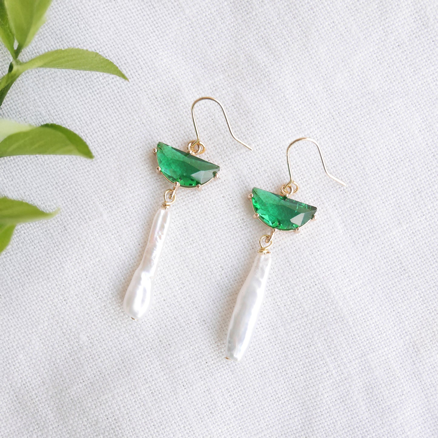Green biwa pearl earrings on a white cloth.