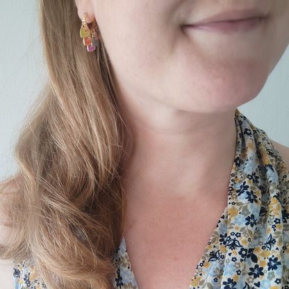 Woman wearing colorful heart cluster hoop earrings.