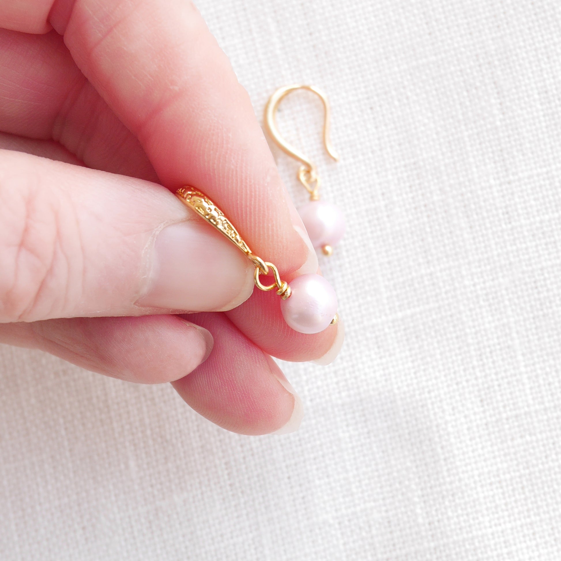 Fingers of a woman holding a baroque freshwater pearl earring.