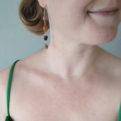Woman wearing long jasper stone dangle earrings.