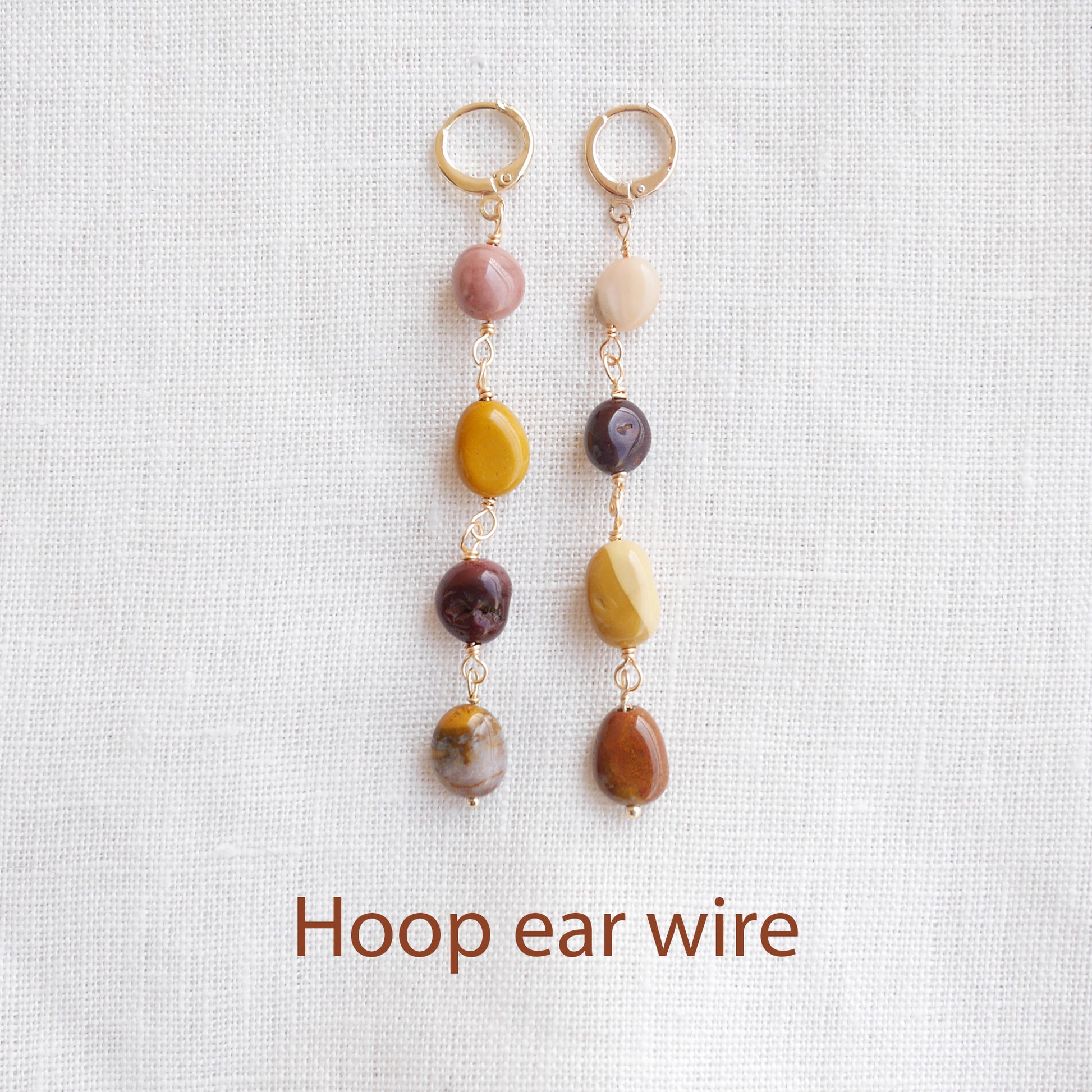 Long jasper stone dangle earrings in earthy mookaite colors, on a white cloth.