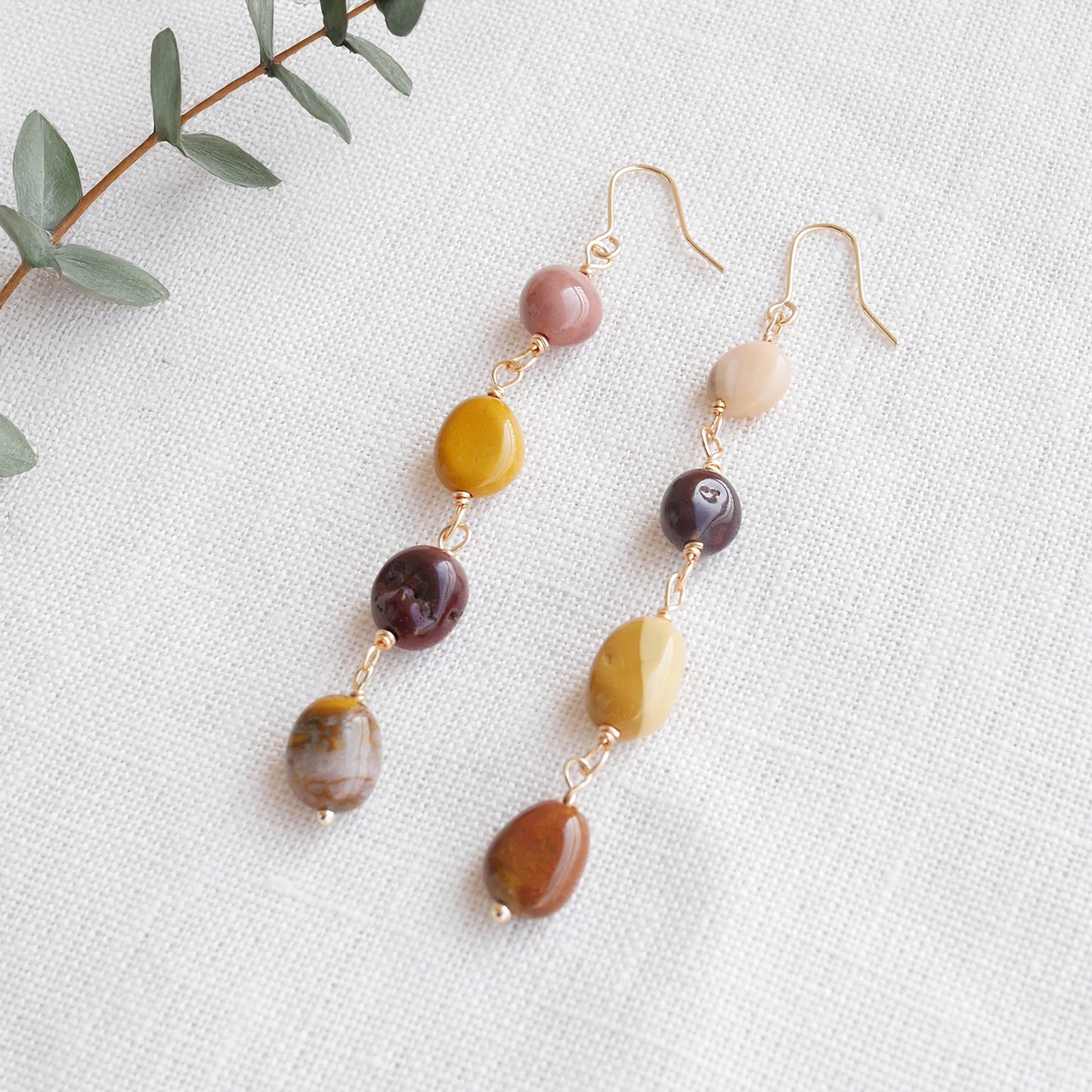 Long jasper stone dangle earrings in earthy mookaite colors, on a white cloth.