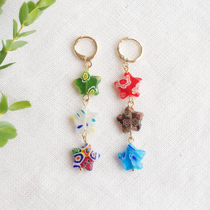 Colorful star dangle earrings with three millefiori star shape glass beads in each earring, on a white cloth.