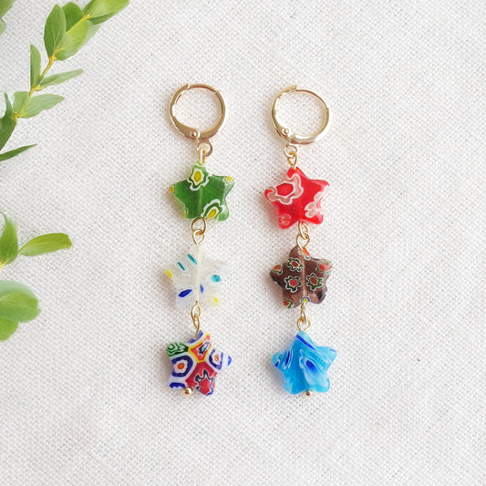 Colorful star dangle earrings with three millefiori star shape glass beads in each earring, on a white cloth.