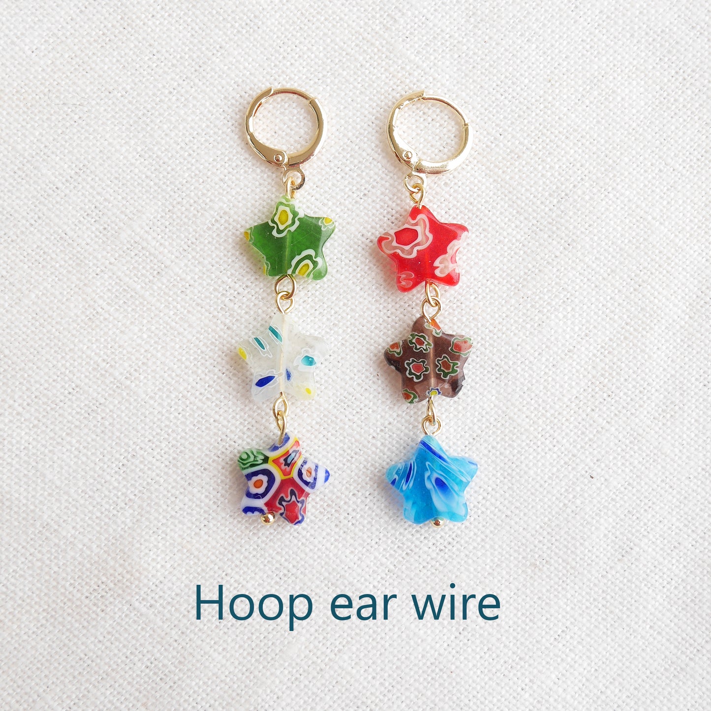 Colorful star dangle earrings with three millefiori star shape glass beads in each earring, on a white cloth.
