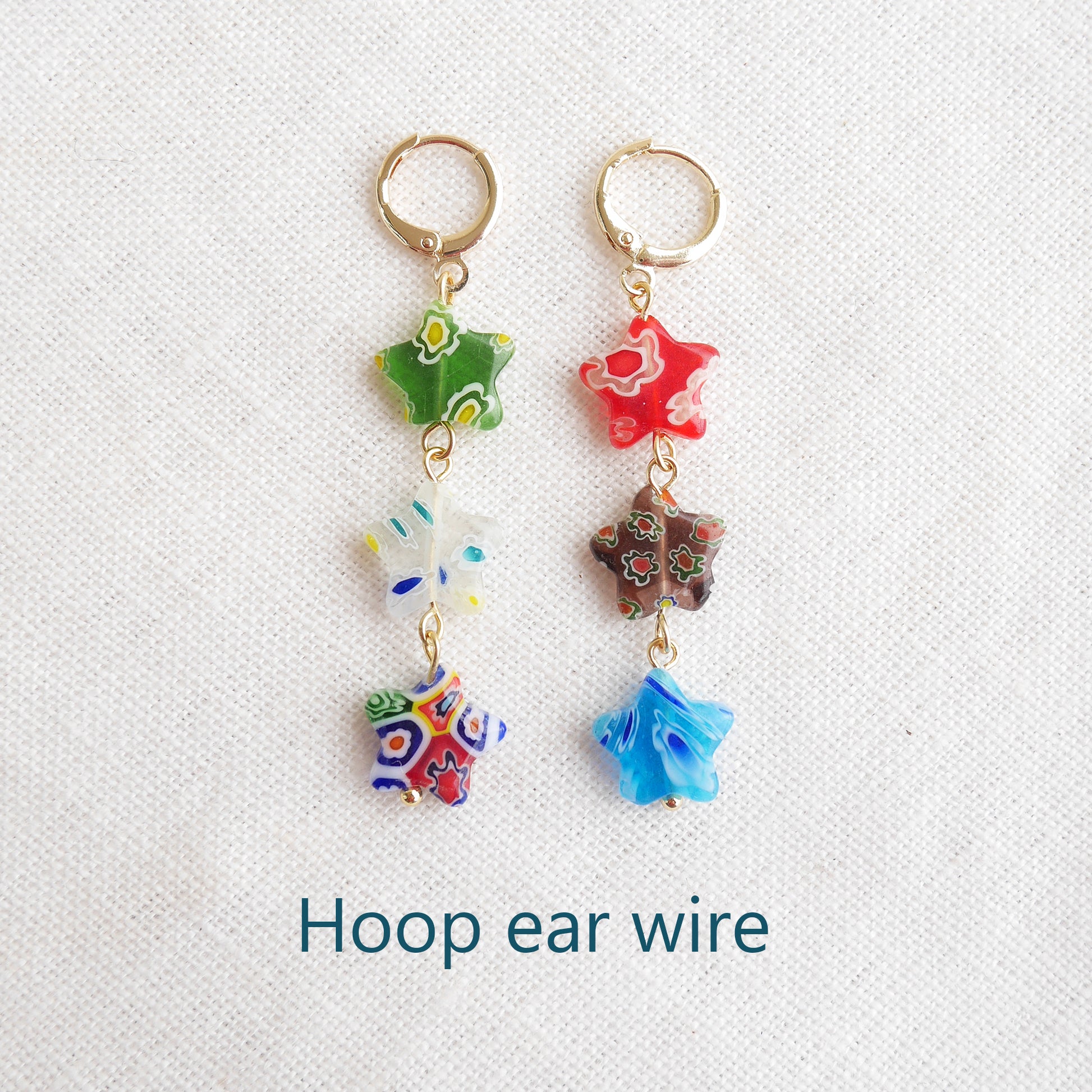 Colorful star dangle earrings with three millefiori star shape glass beads in each earring, on a white cloth.