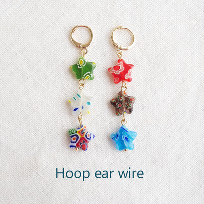 Colorful star dangle earrings with three millefiori star shape glass beads in each earring, on a white cloth.