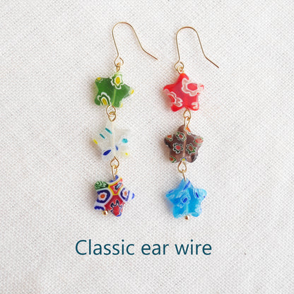 Colorful star dangle earrings with three millefiori star shape glass beads in each earring, on a white cloth.