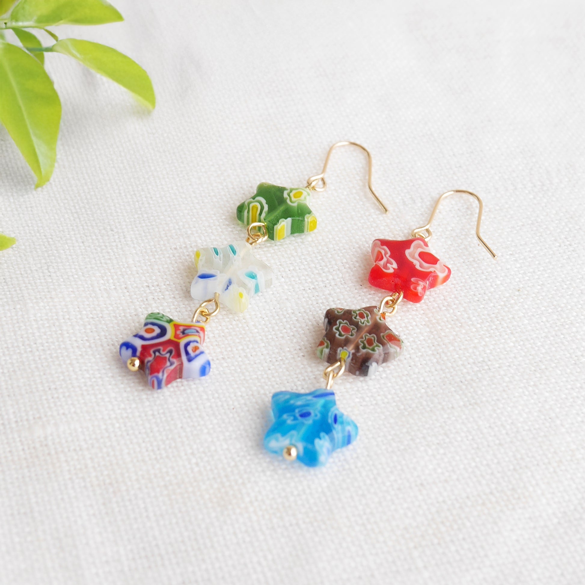Colorful star dangle earrings with three millefiori star shape glass beads in each earring, on a white cloth.