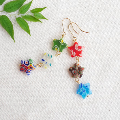 Colorful star dangle earrings with three millefiori star shape glass beads in each earring, on a white cloth.