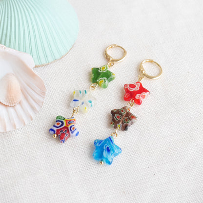 Colorful star dangle earrings with three millefiori star shape glass beads in each earring, on a white cloth.