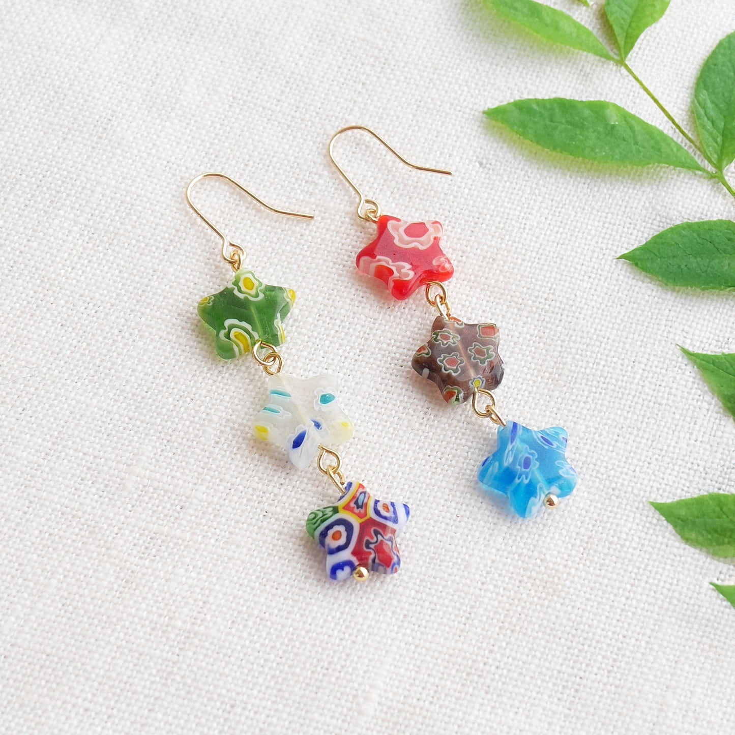 Colorful star dangle earrings with three millefiori star shape glass beads in each earring, on a white cloth.