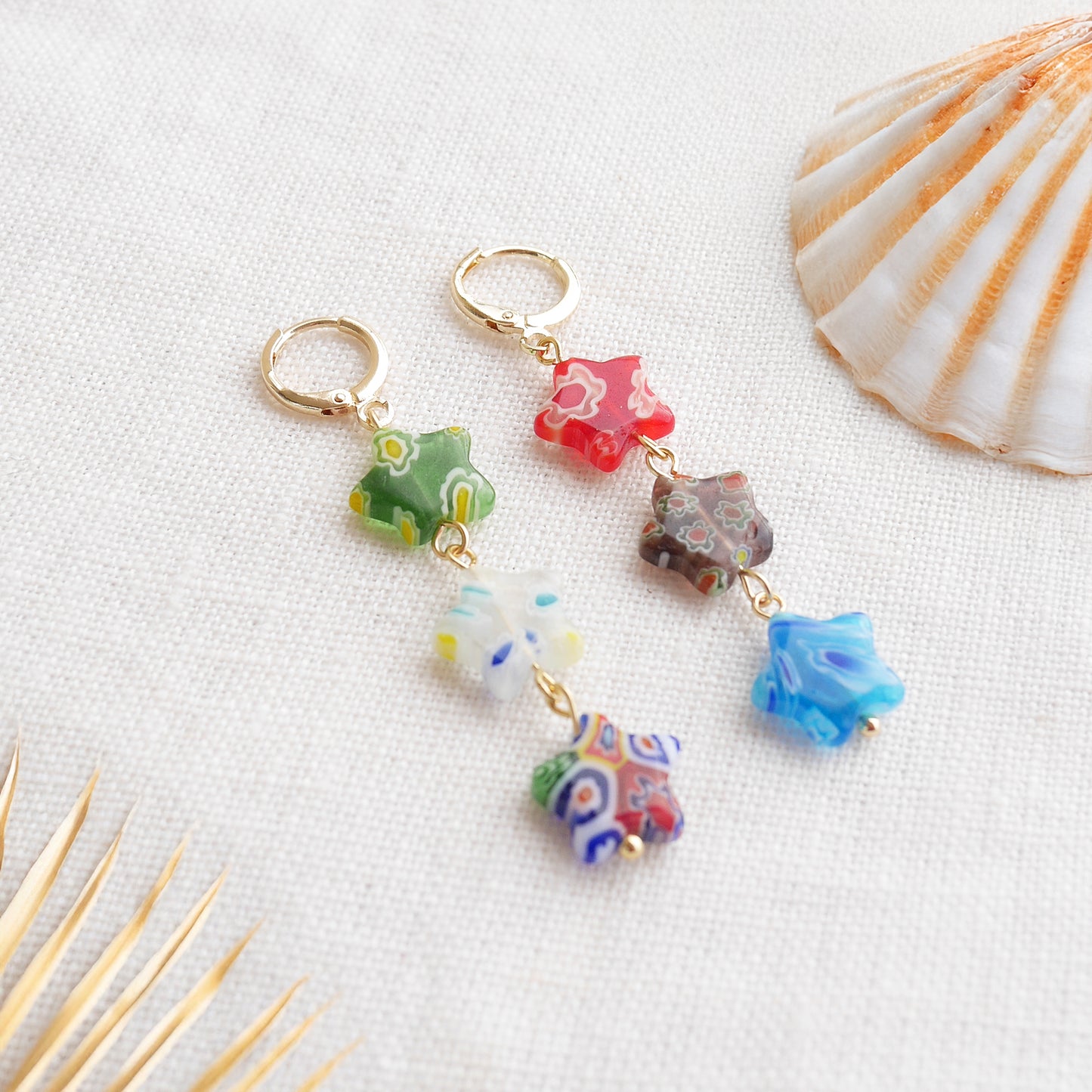 Colorful star dangle earrings with three millefiori star shape glass beads in each earring, on a white cloth.