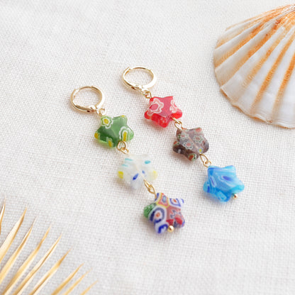 Colorful star dangle earrings with three millefiori star shape glass beads in each earring, on a white cloth.