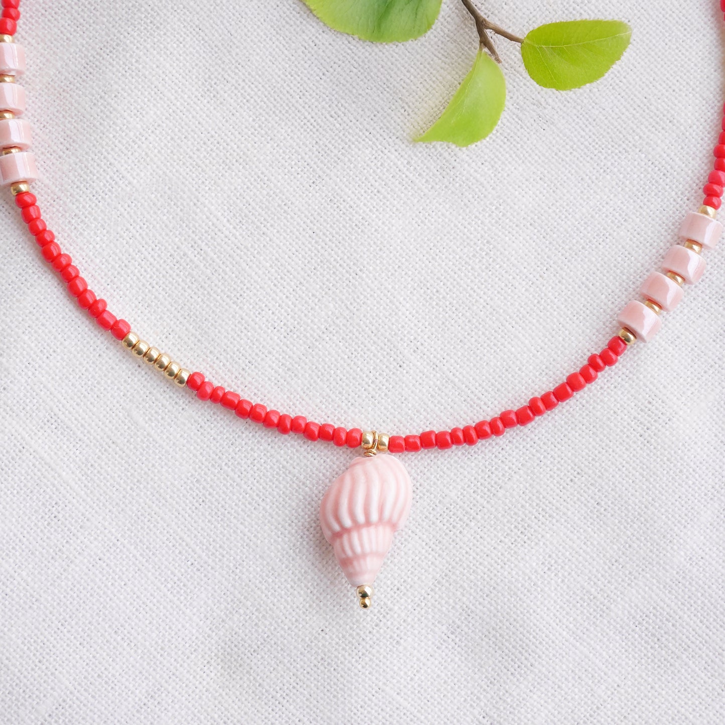 Beaded red conch shell necklace, on a white cloth.