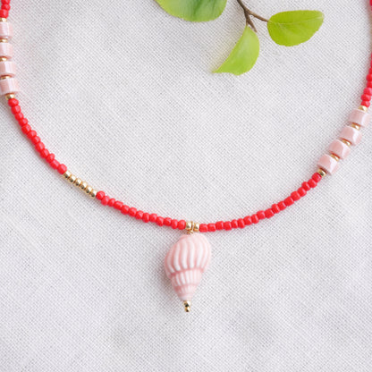 Beaded red conch shell necklace, on a white cloth.