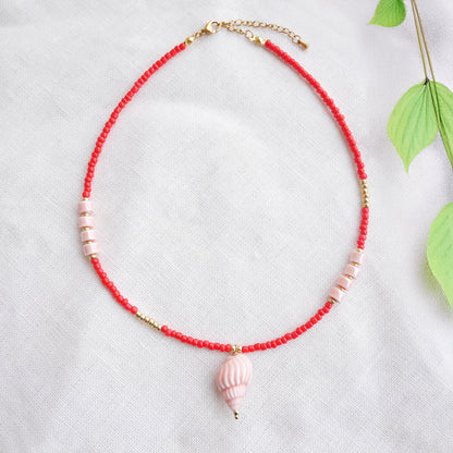 Beaded red conch shell necklace, on a white cloth.