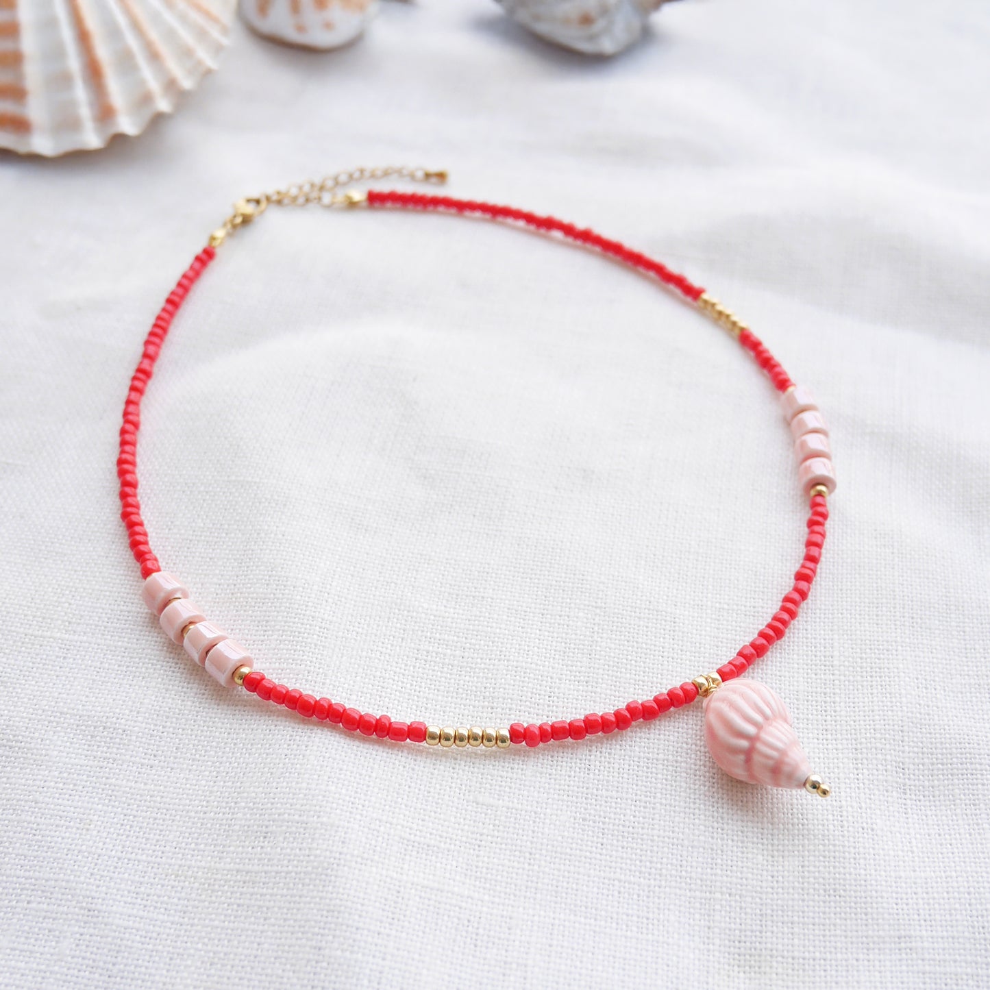 Beaded red conch shell necklace, on a white cloth.