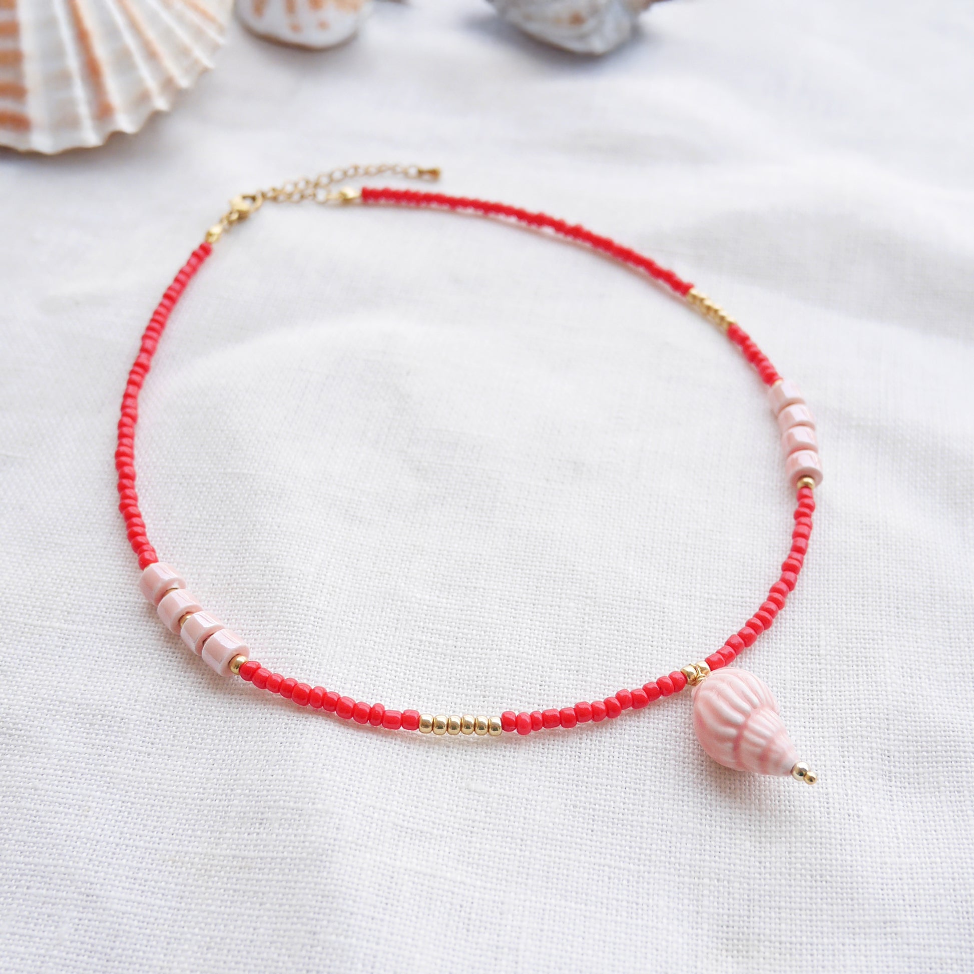 Beaded red conch shell necklace, on a white cloth.
