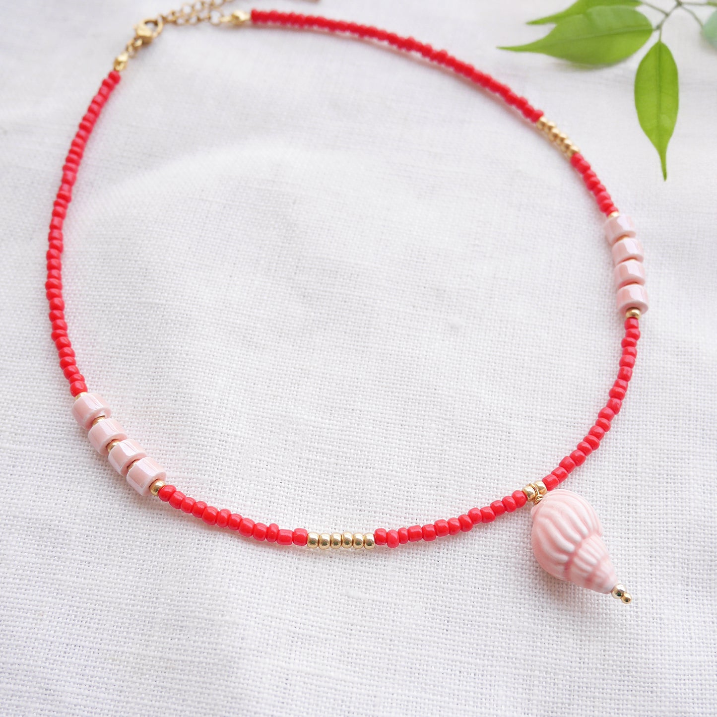 Beaded red conch shell necklace, on a white cloth.