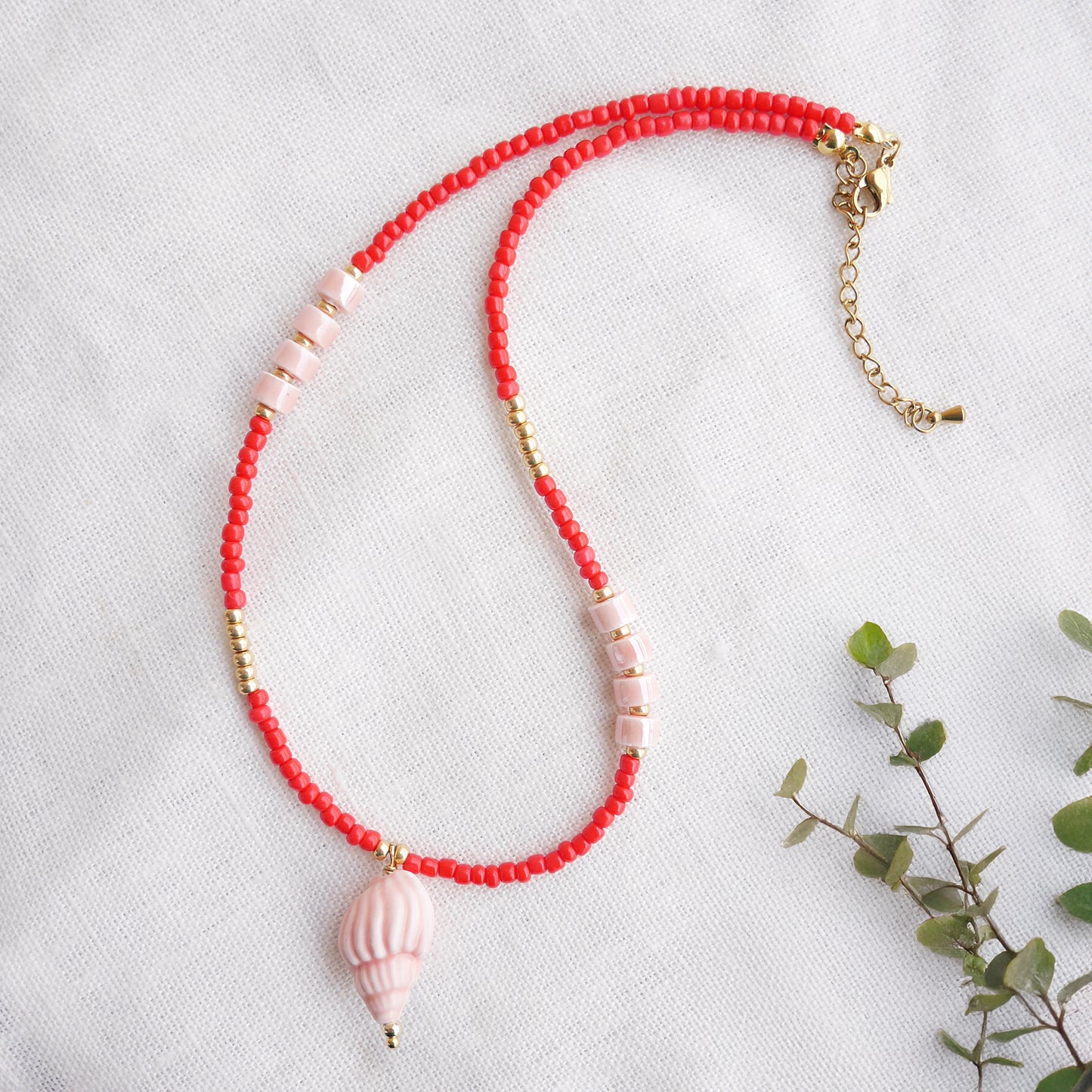 Beaded red conch shell necklace, on a white cloth.
