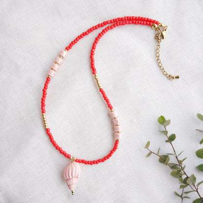 Beaded red conch shell necklace, on a white cloth.