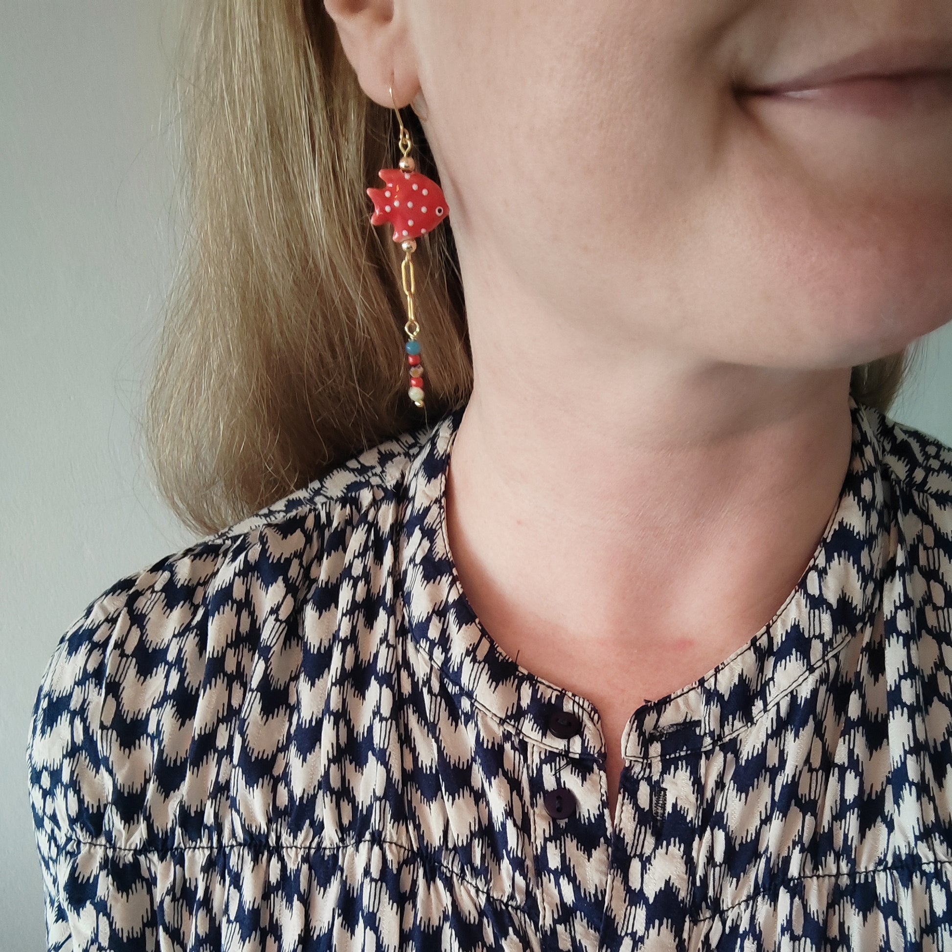 Woman wearing red fish dangle earrings.