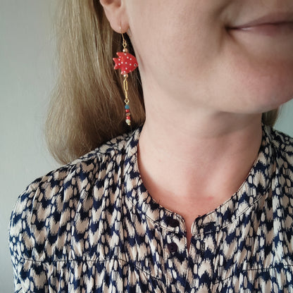 Woman wearing red fish dangle earrings.
