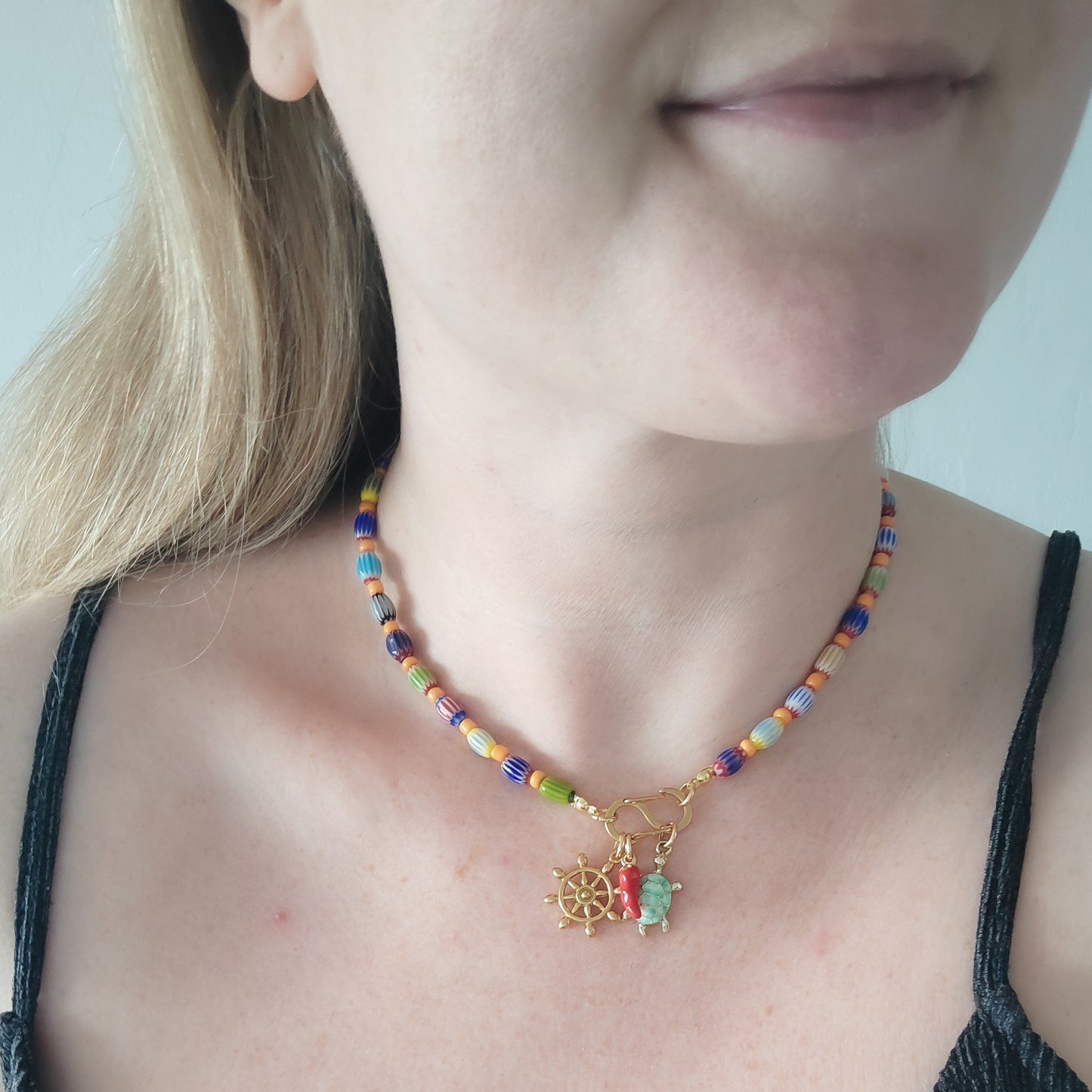 Woman wearing a colorful beaded necklace with S shape front clasp lock and three charms.