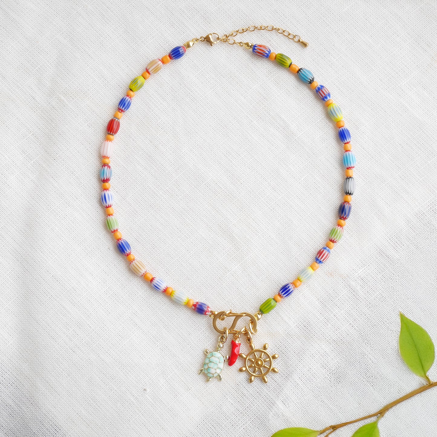 Colorful beaded necklace with S shape front clasp lock and three charms, on a white cloth.