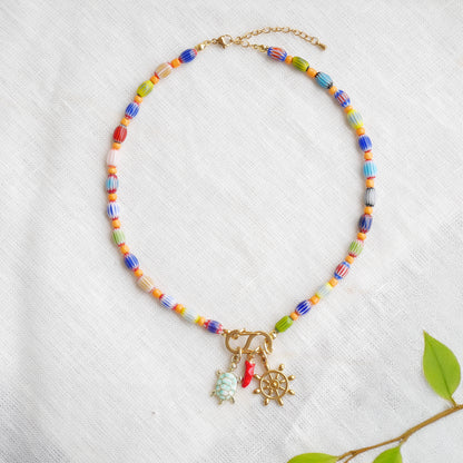 Colorful beaded necklace with S shape front clasp lock and three charms, on a white cloth.