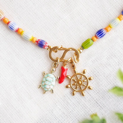 Colorful beaded necklace with S shape front clasp lock and three charms, on a white cloth.