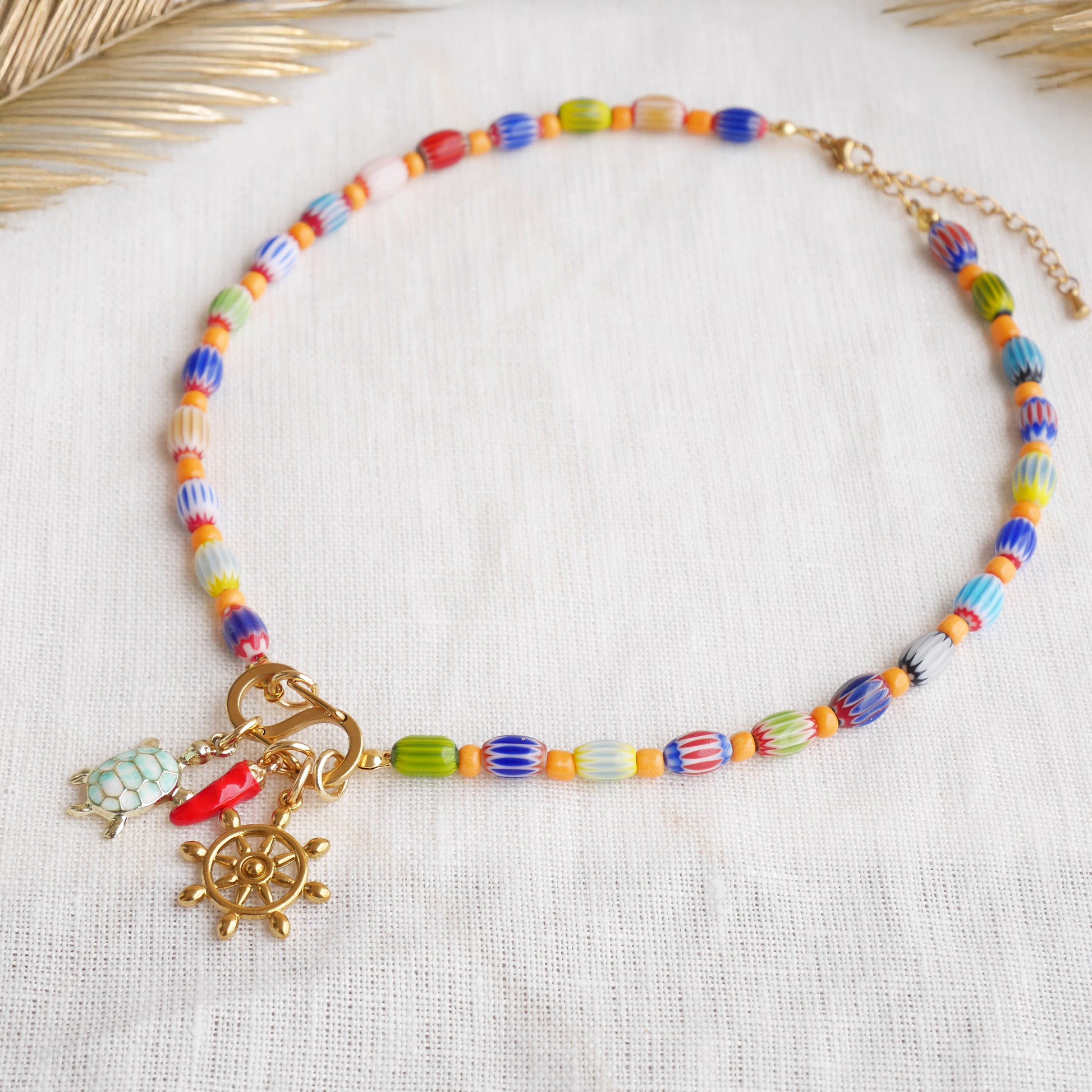 Colorful beaded necklace with S shape front clasp lock and three charms, on a white cloth.