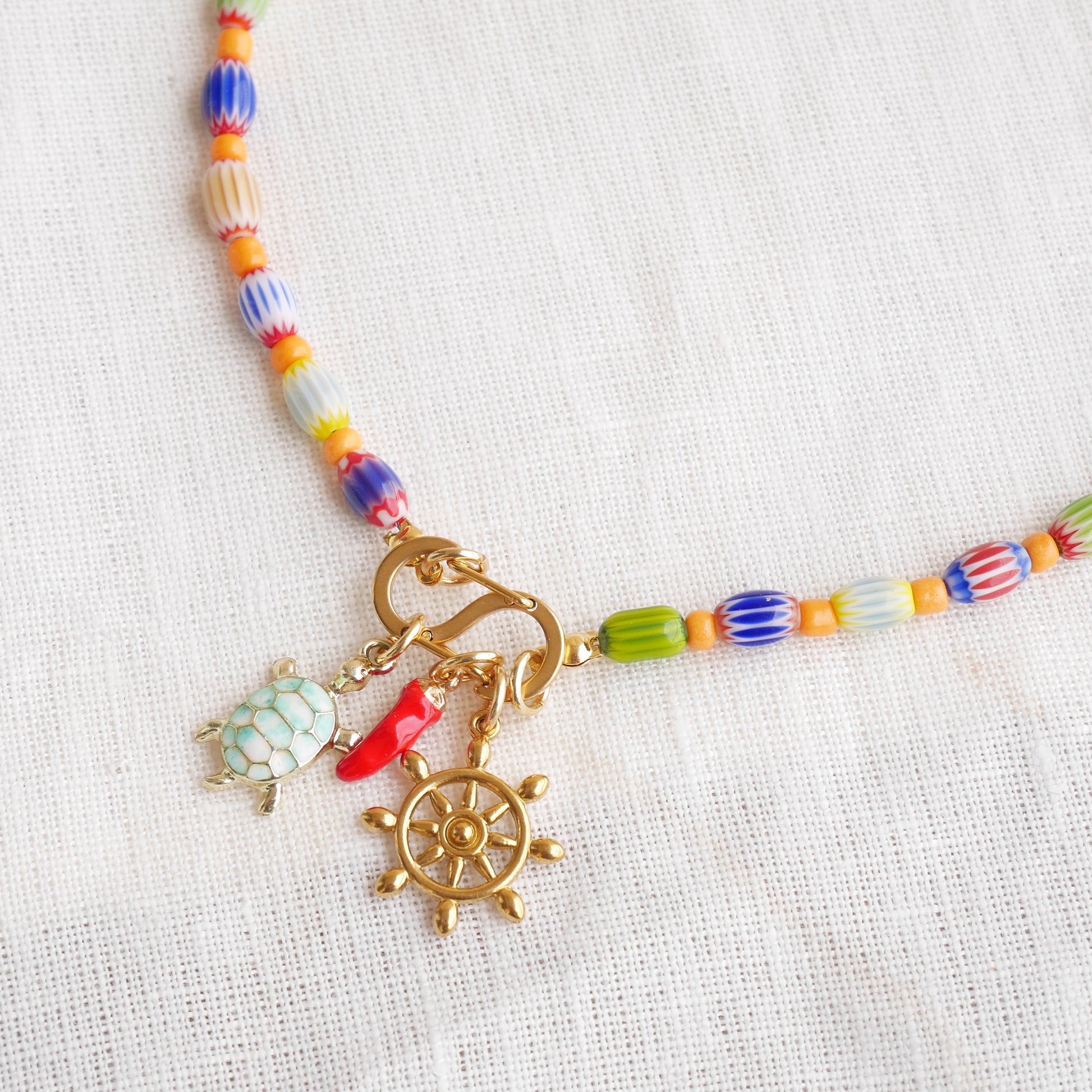 Colorful beaded necklace with S shape front clasp lock and three charms, on a white cloth.