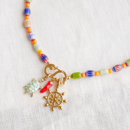 Colorful beaded necklace with S shape front clasp lock and three charms, on a white cloth.