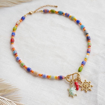 Colorful beaded necklace with S shape front clasp lock and three charms, on a white cloth.