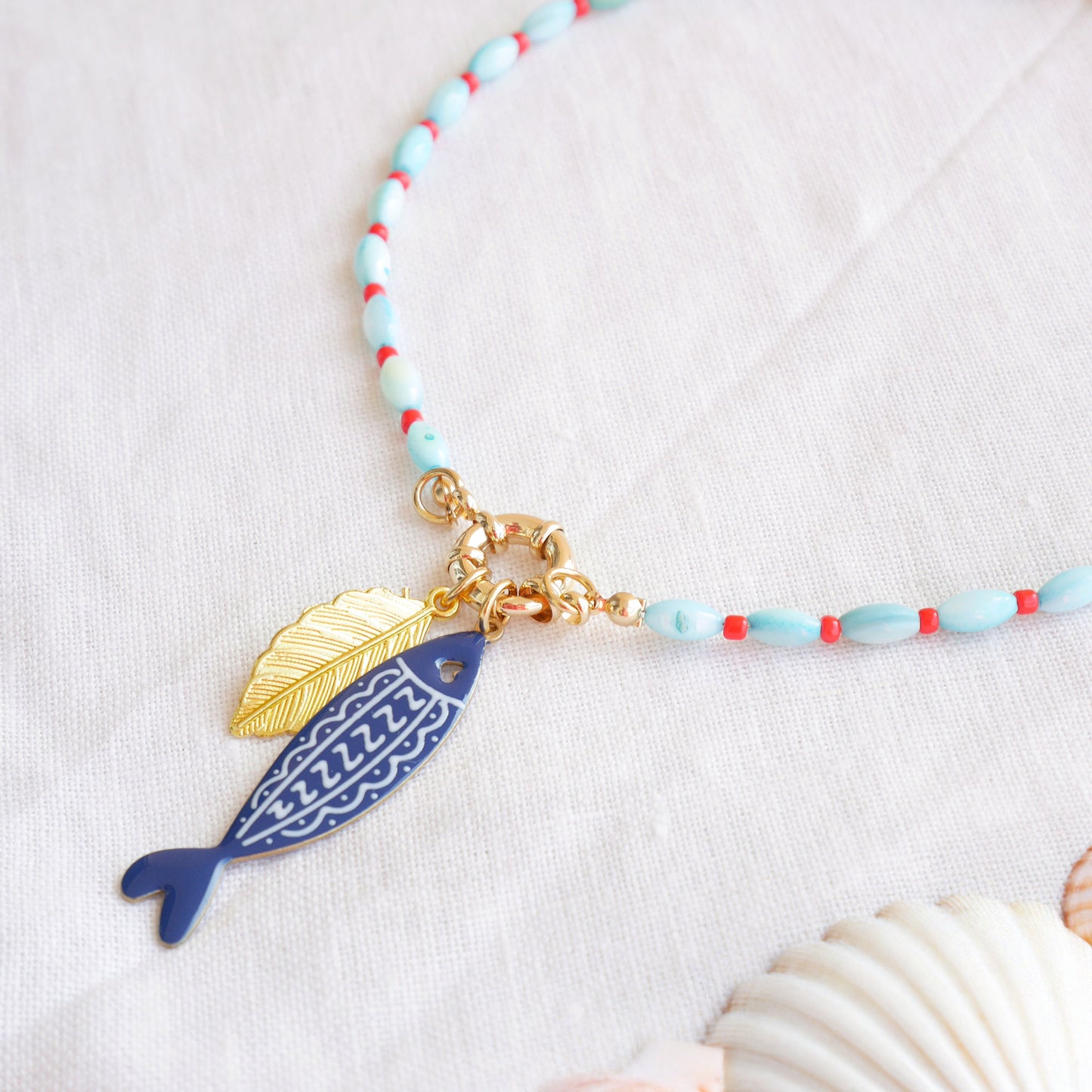Turquoise red beaded necklace with fish and leaf charm on a white cloth.