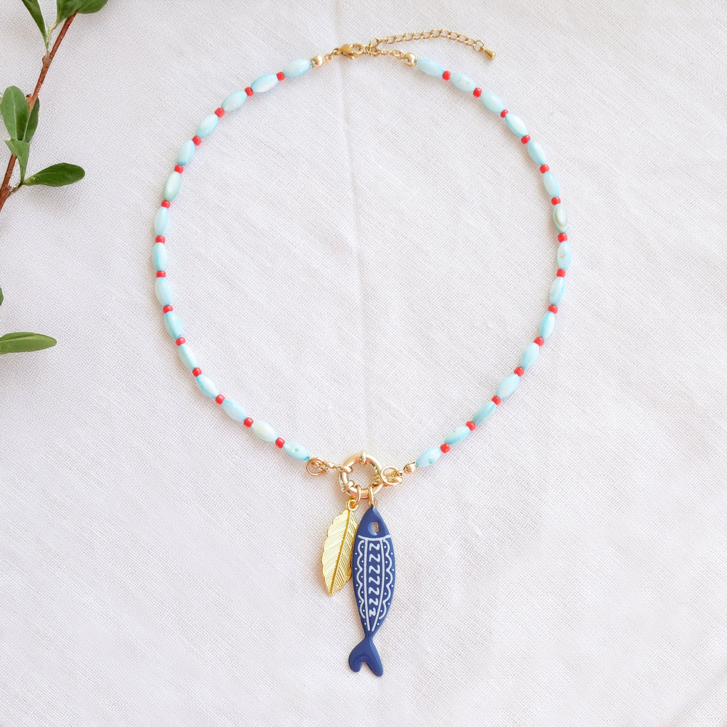Turquoise red beaded necklace with fish and leaf charm on a white cloth.