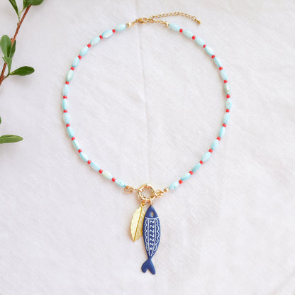 Turquoise red beaded necklace with fish and leaf charm on a white cloth.