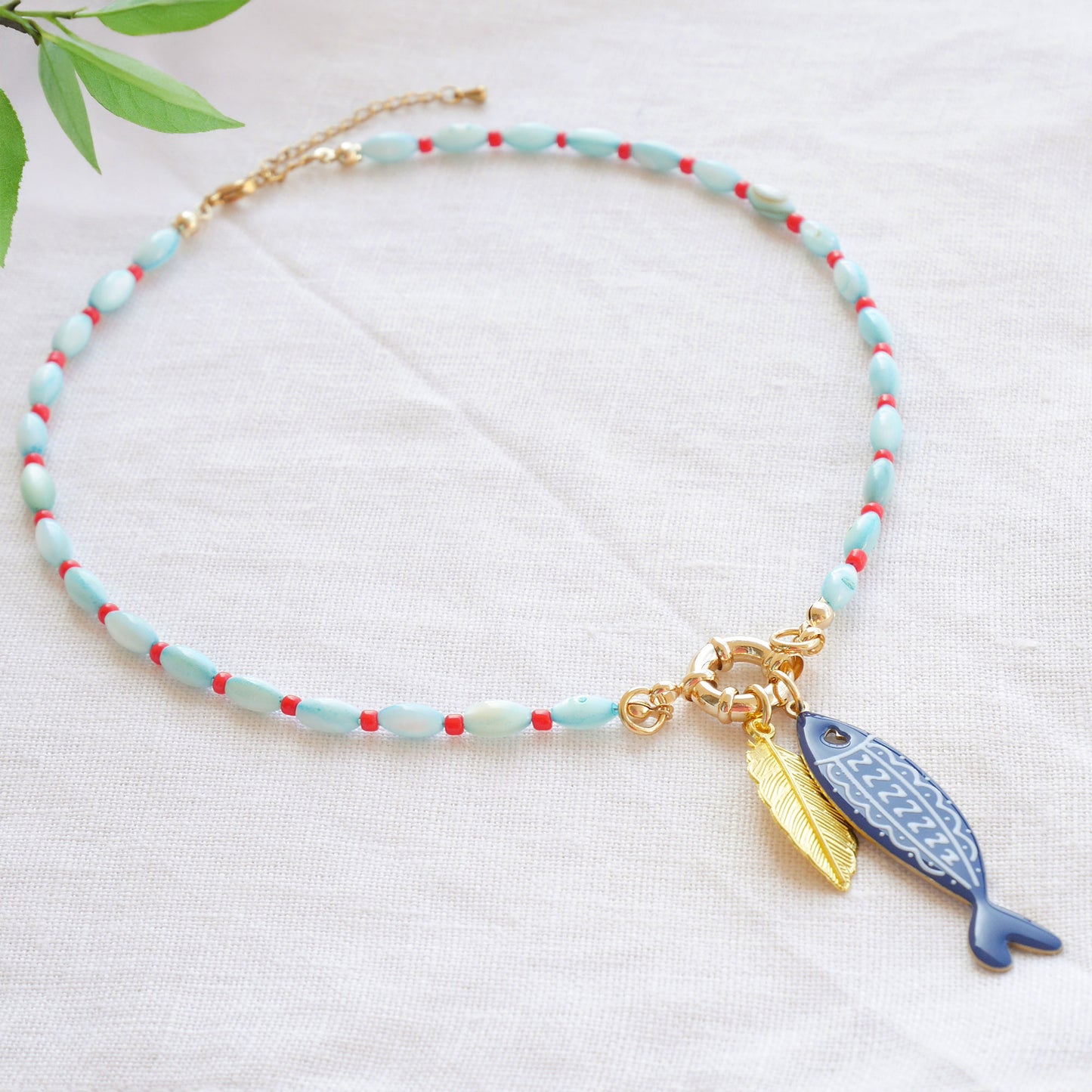 Turquoise red beaded necklace with fish and leaf charm on a white cloth.