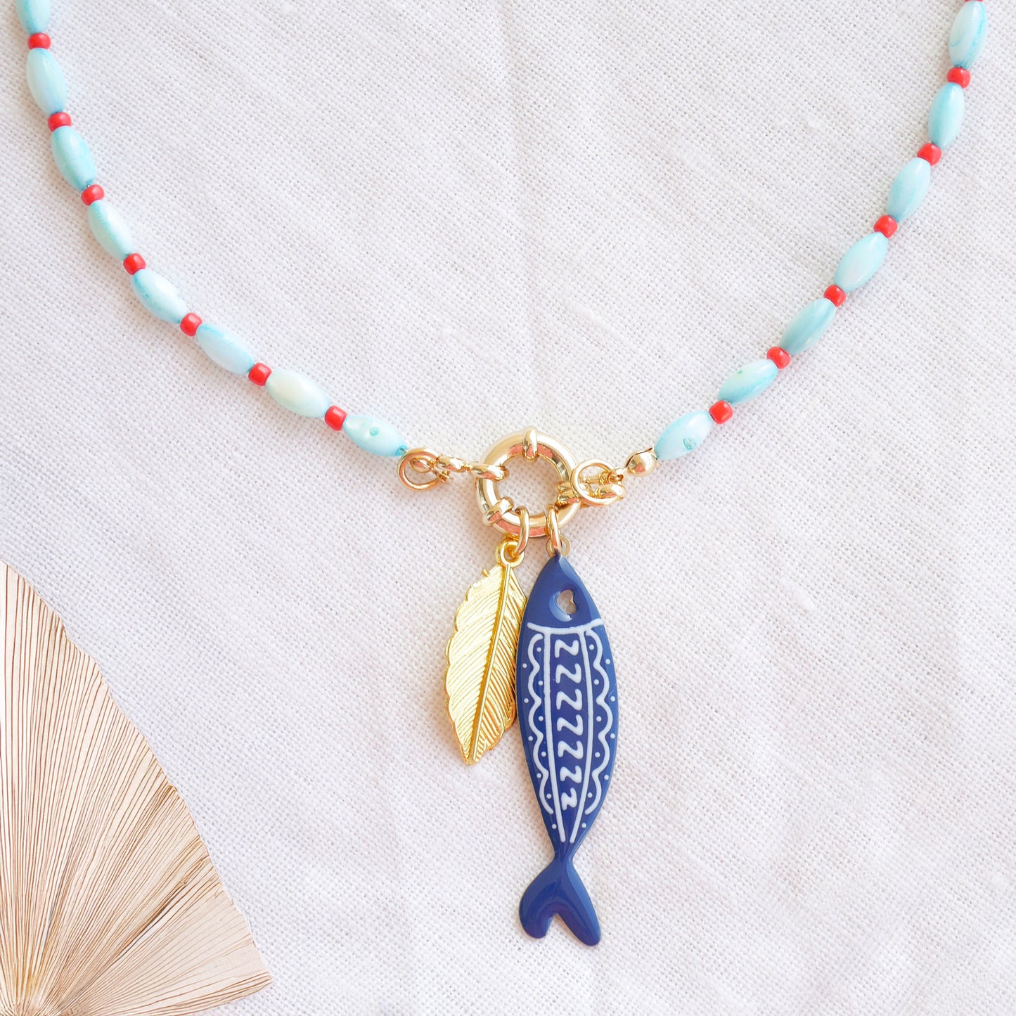 Turquoise red beaded necklace with fish and leaf charm on a white cloth.