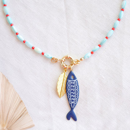 Turquoise red beaded necklace with fish and leaf charm on a white cloth.