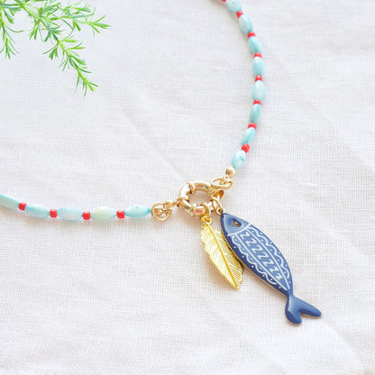 Turquoise red beaded necklace with fish and leaf charm on a white cloth.