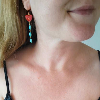 Woman wearing long dangle earrings with red porcelain hearts and turquoise shell beads.