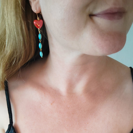 Woman wearing long dangle earrings with red porcelain hearts and turquoise shell beads.