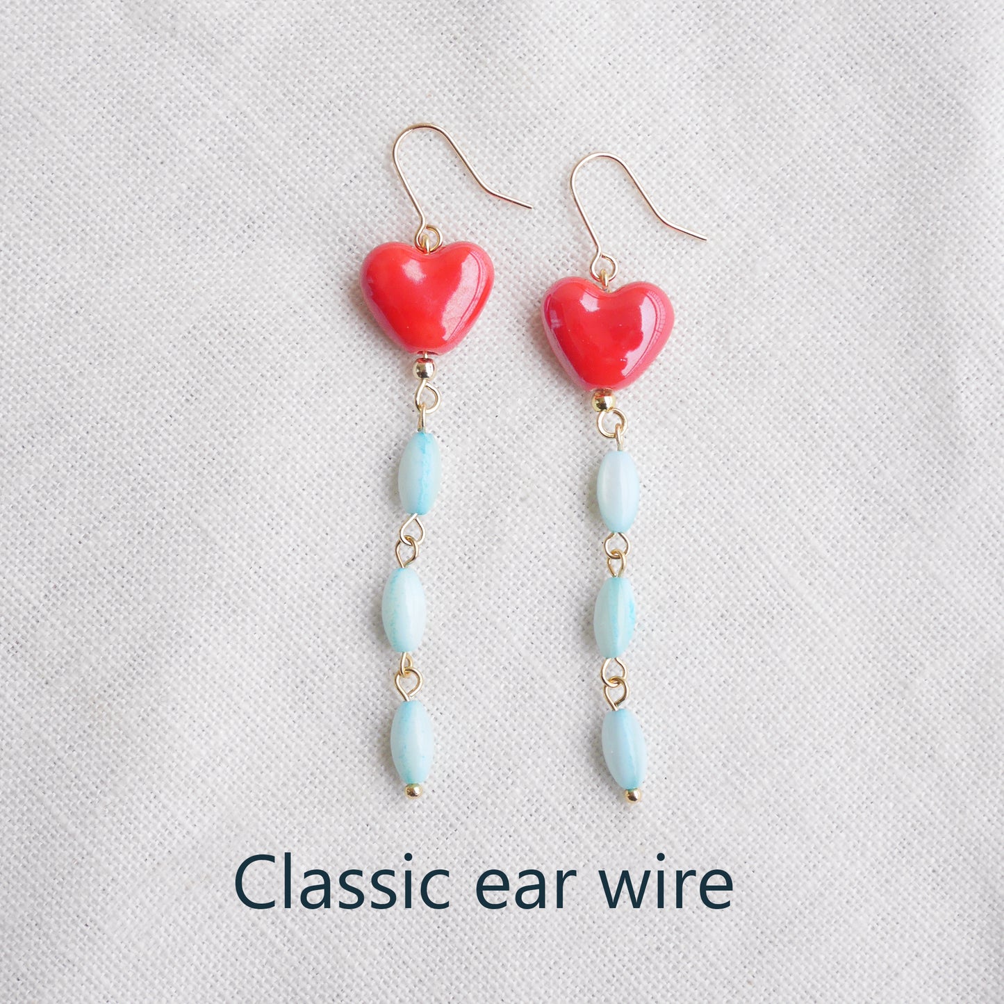 Long dangle earrings with red porcelain hearts and turquoise shell beads, on a white cloth.