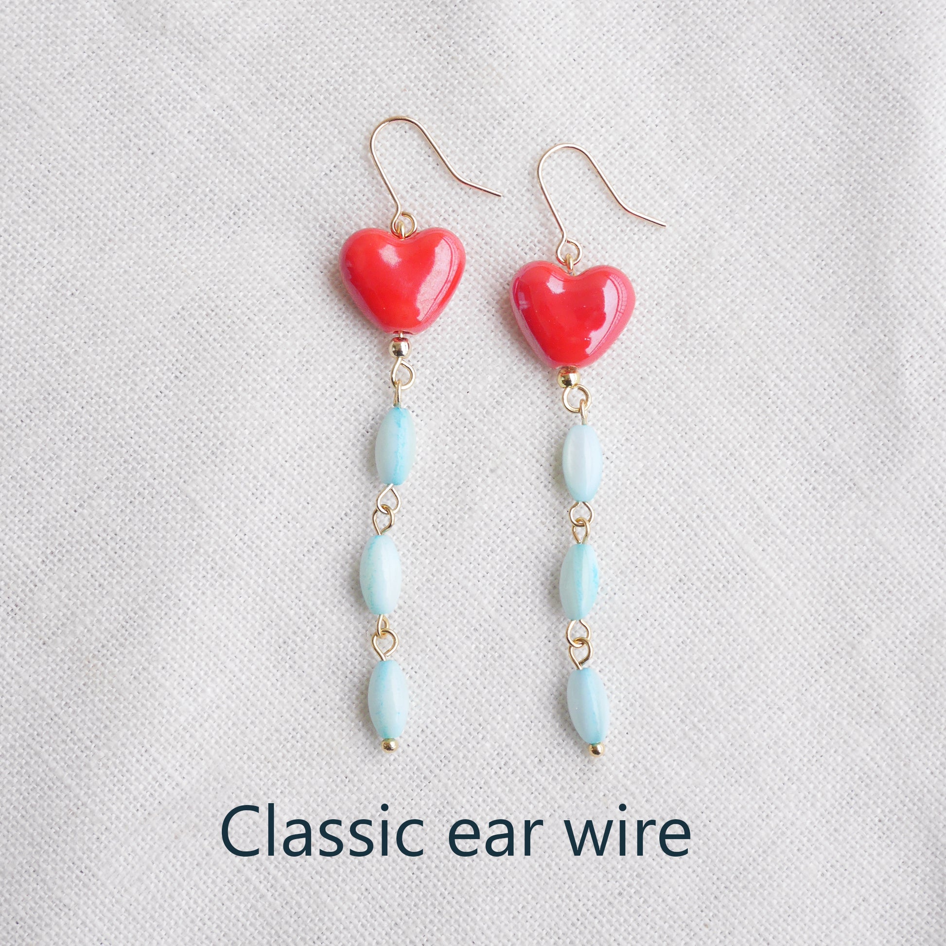 Long dangle earrings with red porcelain hearts and turquoise shell beads, on a white cloth.
