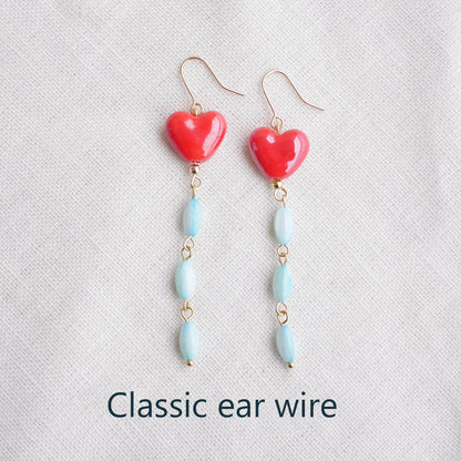 Long dangle earrings with red porcelain hearts and turquoise shell beads, on a white cloth.